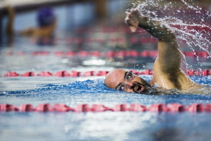 Male with clear googles and a brown beard taking a breath while swimming freestyle