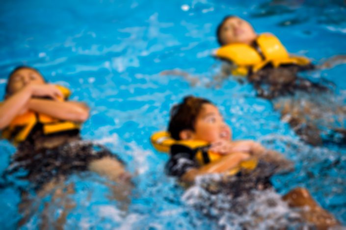 Kids floating in life jackets in pool